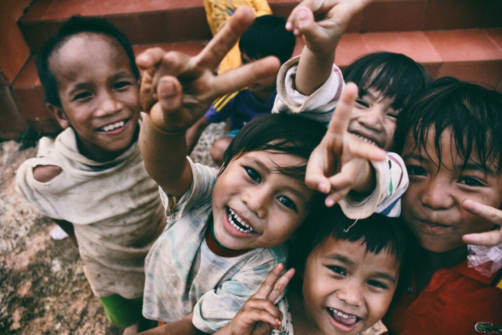 A group of smiling children, holding up the peace sign.