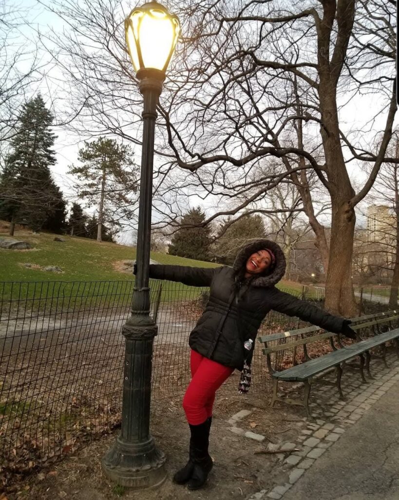 A woman holding on to a lamp post in Central Park, NY.