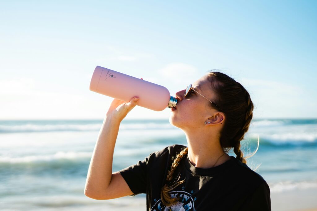 Traveler drinking from a reusable water bottle at the beach